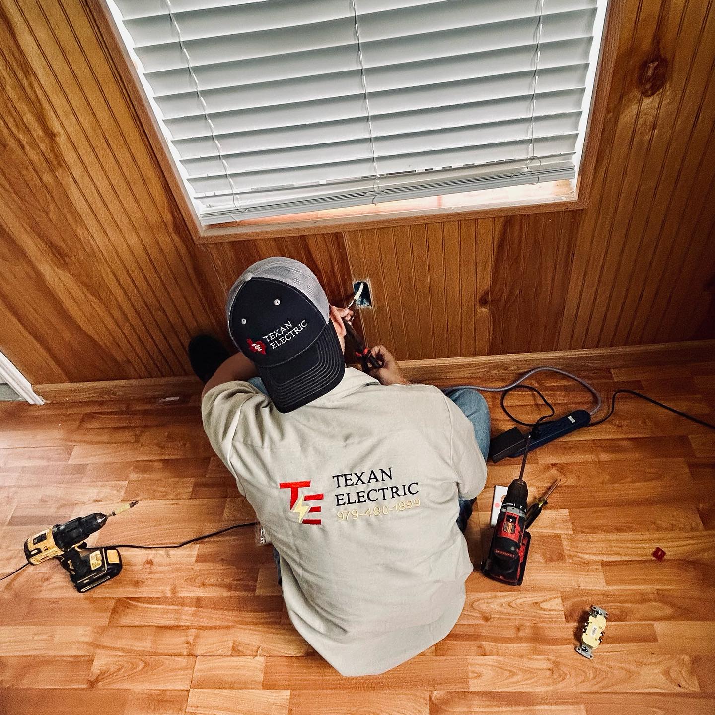 Texan Electric technician in branded uniform installing a new electrical outlet on a hardwood floor
