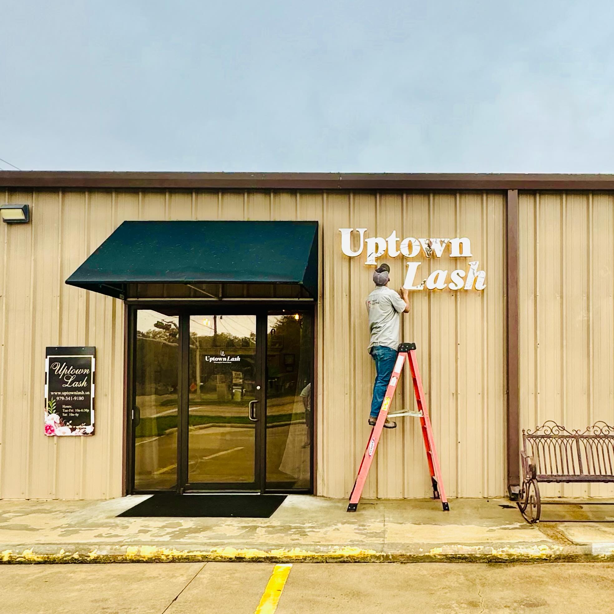 Texan Electric technician on a ladder installing storefront sign and awning lighting at Uptown Lash